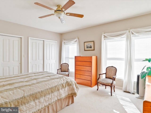 carpeted bedroom with a ceiling fan and multiple closets