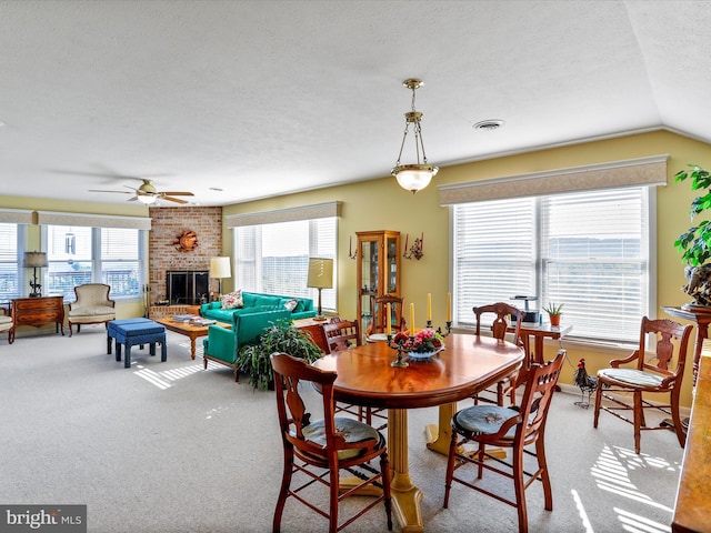 carpeted dining space with a textured ceiling, a healthy amount of sunlight, a ceiling fan, and a brick fireplace