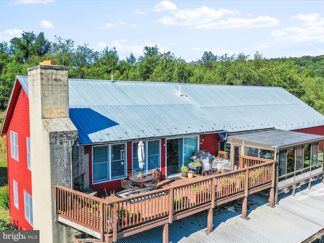 rear view of property featuring a chimney, outdoor dining space, a deck, and metal roof