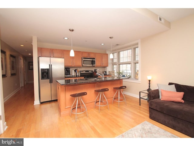 kitchen with dark stone countertops, light hardwood / wood-style flooring, appliances with stainless steel finishes, pendant lighting, and a kitchen bar