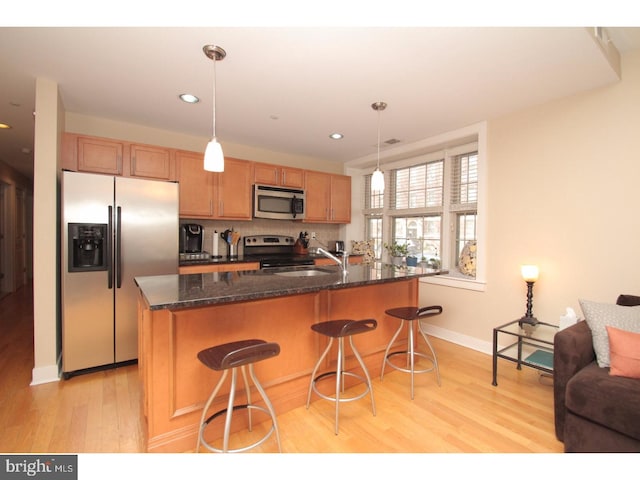 kitchen featuring appliances with stainless steel finishes, decorative light fixtures, light wood-type flooring, and dark stone counters