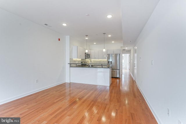 kitchen with decorative light fixtures, appliances with stainless steel finishes, kitchen peninsula, white cabinets, and backsplash