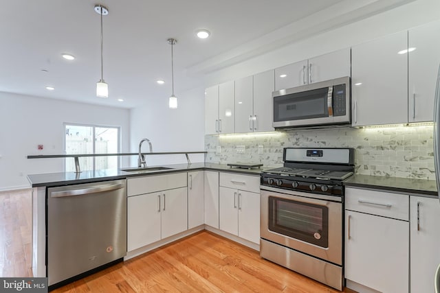 kitchen with sink, white cabinetry, hanging light fixtures, appliances with stainless steel finishes, and light hardwood / wood-style floors