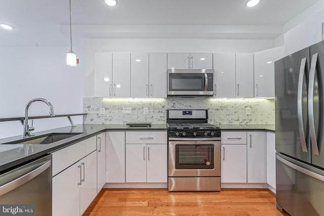 kitchen with pendant lighting, sink, appliances with stainless steel finishes, light hardwood / wood-style floors, and white cabinets