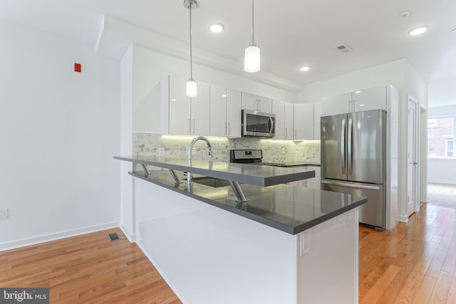 kitchen with appliances with stainless steel finishes, hanging light fixtures, white cabinets, kitchen peninsula, and light wood-type flooring