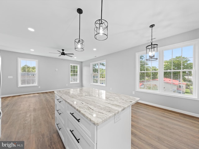 kitchen with white cabinets, ceiling fan with notable chandelier, a kitchen island, wood-type flooring, and decorative light fixtures