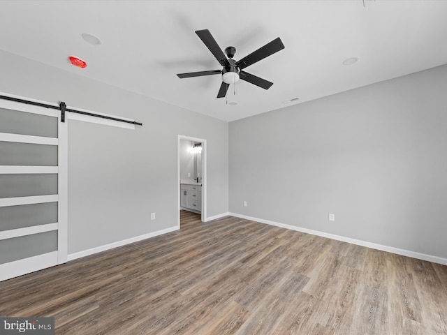 empty room featuring a barn door, ceiling fan, and hardwood / wood-style floors