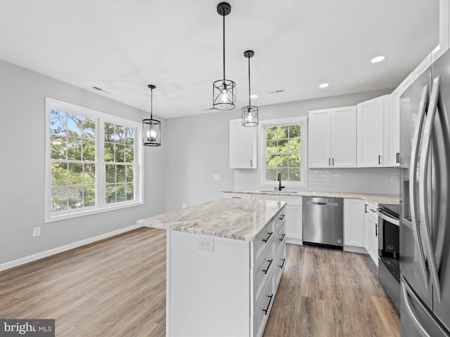 kitchen with a center island, light hardwood / wood-style floors, hanging light fixtures, appliances with stainless steel finishes, and sink