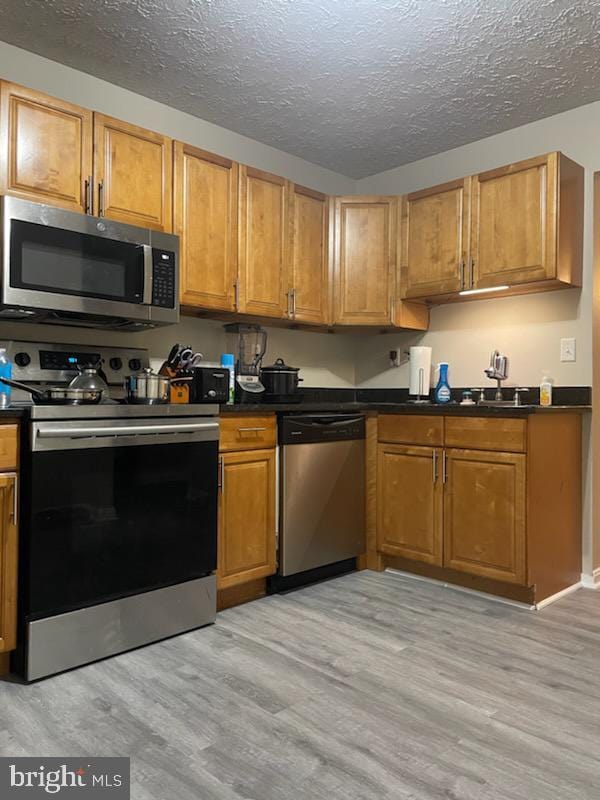 kitchen featuring stainless steel appliances, sink, a textured ceiling, and light hardwood / wood-style flooring