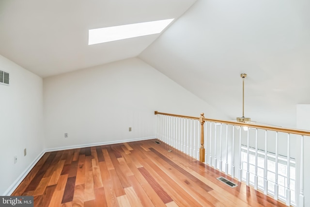 additional living space with hardwood / wood-style flooring, vaulted ceiling with skylight, and ceiling fan