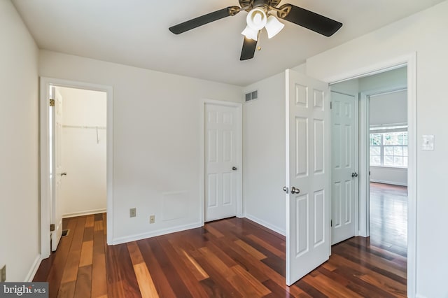 unfurnished bedroom featuring ceiling fan, dark hardwood / wood-style floors, a walk in closet, and a closet