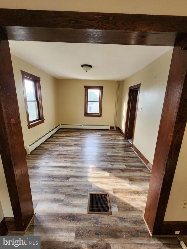 unfurnished room featuring a baseboard heating unit, hardwood / wood-style floors, and a wealth of natural light