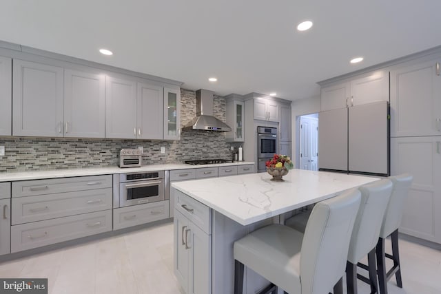 kitchen with white fridge, wall chimney range hood, a center island, gray cabinets, and decorative backsplash