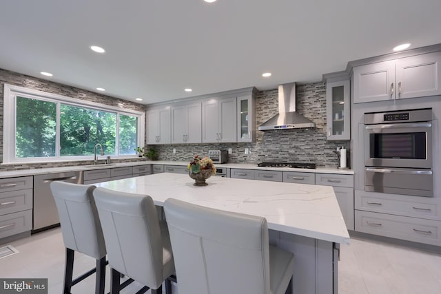 kitchen with appliances with stainless steel finishes, tasteful backsplash, wall chimney range hood, light tile patterned flooring, and a center island