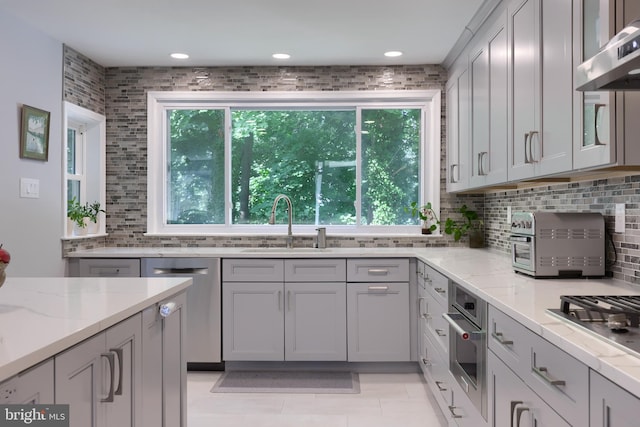 kitchen featuring wall chimney range hood, sink, light stone countertops, and backsplash