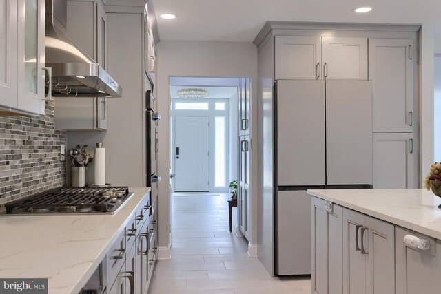 kitchen featuring stainless steel appliances, tasteful backsplash, wall chimney range hood, and light stone countertops