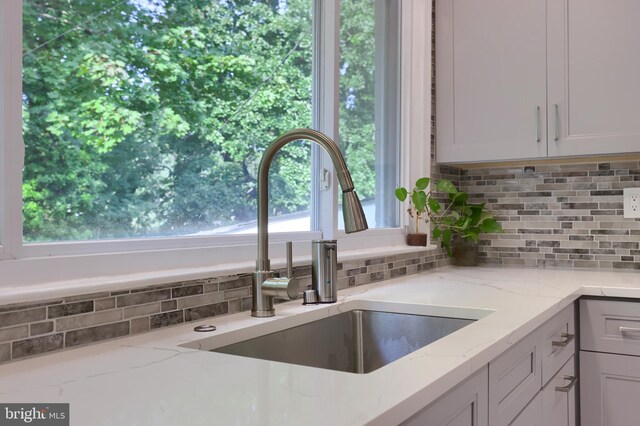 kitchen featuring white cabinetry, backsplash, light stone counters, and sink