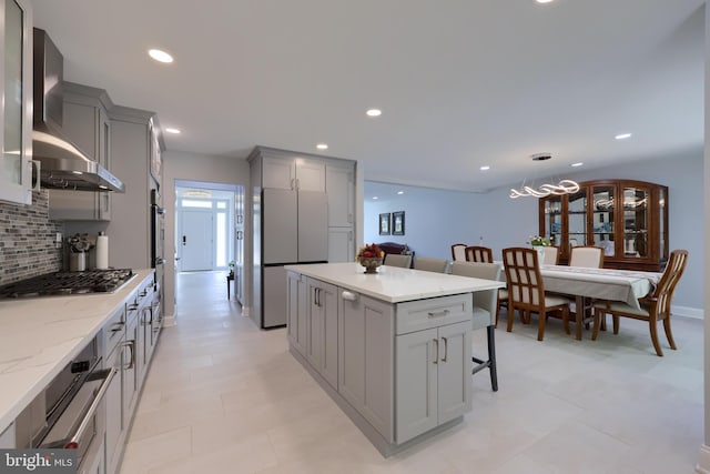 kitchen with tasteful backsplash, wall chimney range hood, pendant lighting, a breakfast bar, and appliances with stainless steel finishes