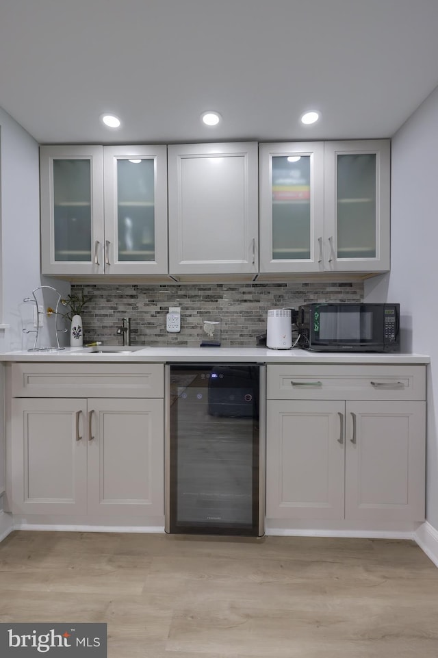 bar featuring decorative backsplash, light wood-type flooring, dishwashing machine, and white cabinetry