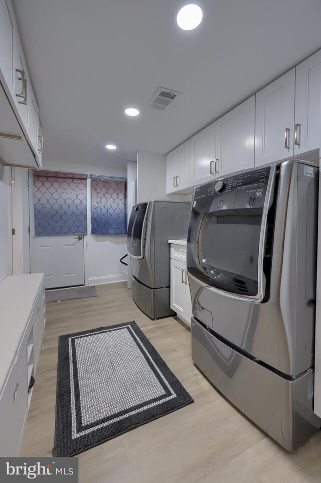 clothes washing area with washing machine and clothes dryer and light wood-type flooring