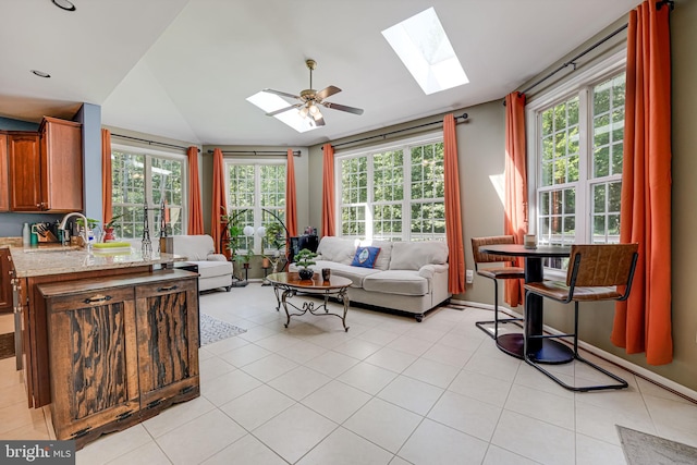 tiled living room featuring ceiling fan, vaulted ceiling with skylight, sink, and a wealth of natural light