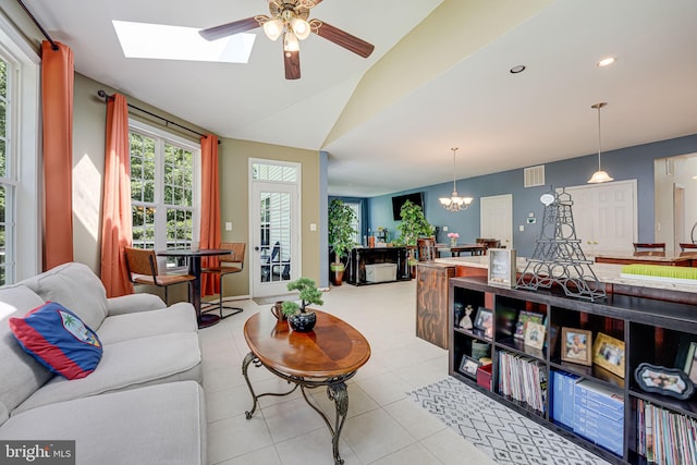 living room featuring lofted ceiling with skylight, ceiling fan with notable chandelier, and light tile patterned floors