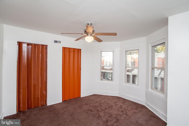 unfurnished bedroom featuring multiple closets, dark carpet, and ceiling fan