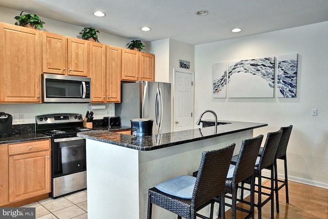 kitchen featuring appliances with stainless steel finishes, a breakfast bar, a kitchen island with sink, and dark stone countertops