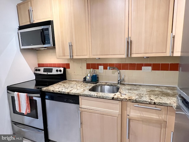 kitchen with decorative backsplash, light stone countertops, appliances with stainless steel finishes, and a sink