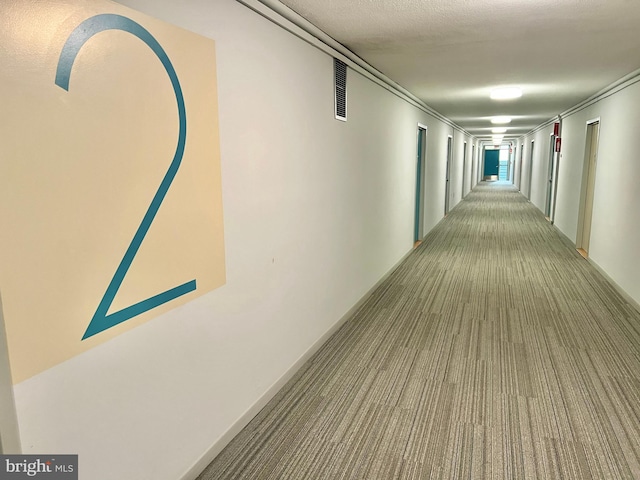 hallway with visible vents, carpet floors, and a textured ceiling