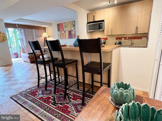 kitchen featuring light brown cabinetry, a kitchen bar, sink, and decorative backsplash