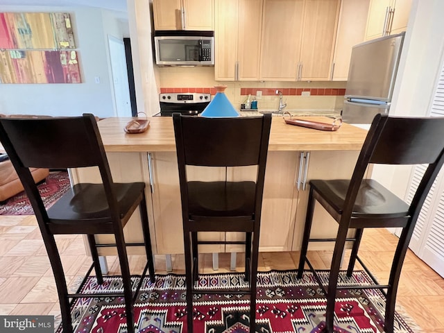 kitchen featuring backsplash, appliances with stainless steel finishes, a breakfast bar area, and wood counters