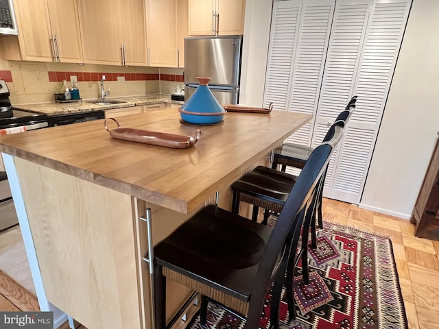 kitchen with a kitchen bar, a sink, tasteful backsplash, stainless steel appliances, and wooden counters