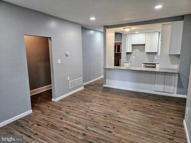 kitchen with dark hardwood / wood-style flooring, white cabinets, dishwasher, light stone counters, and kitchen peninsula