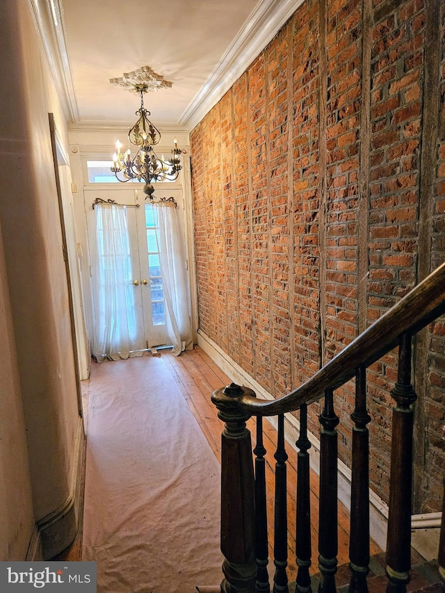 interior space featuring hardwood / wood-style flooring, crown molding, brick wall, and an inviting chandelier