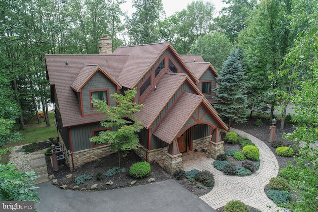 view of front of home with board and batten siding, stone siding, roof with shingles, and a chimney