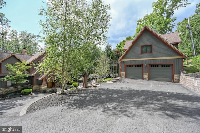 view of side of property with board and batten siding, stone siding, roof with shingles, and a detached garage