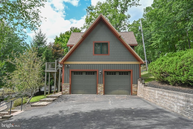 exterior space with stone siding, a detached garage, board and batten siding, and roof with shingles