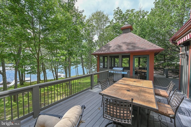 wooden terrace with outdoor dining space, a water view, and a grill