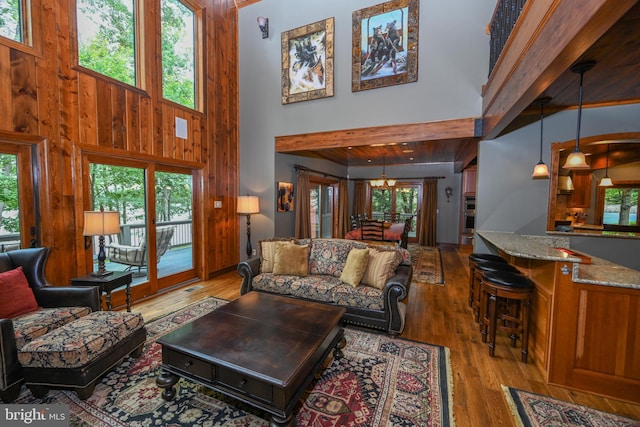 living room with wooden walls, visible vents, a high ceiling, light wood-style floors, and a notable chandelier