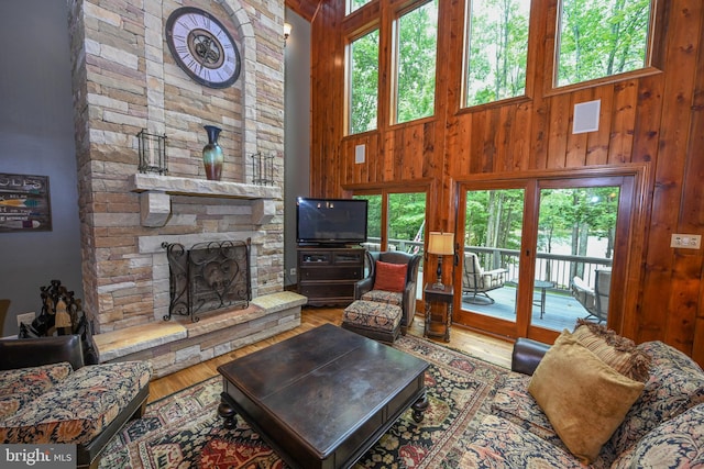 living room featuring hardwood / wood-style floors, a stone fireplace, a high ceiling, wooden walls, and a healthy amount of sunlight