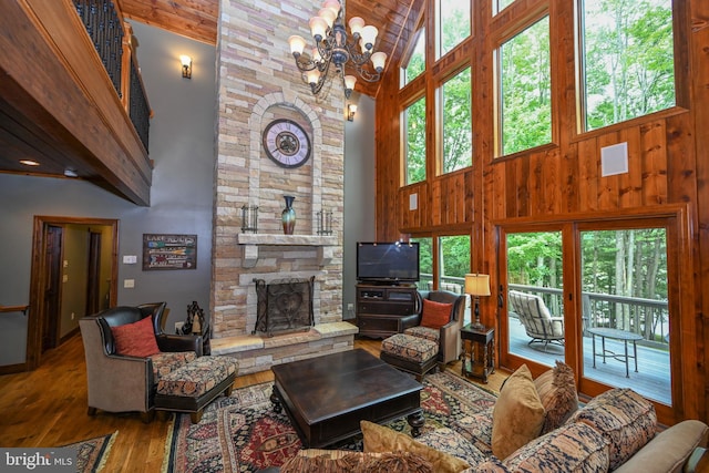 living room with a notable chandelier, plenty of natural light, a stone fireplace, and wood finished floors