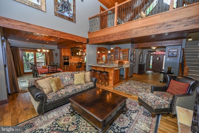 living area with wine cooler, stairway, beamed ceiling, light wood-style floors, and a chandelier