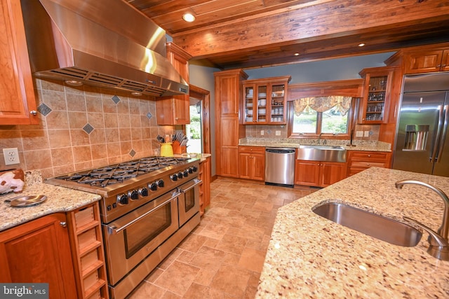 kitchen featuring high end appliances, light stone counters, glass insert cabinets, a sink, and exhaust hood