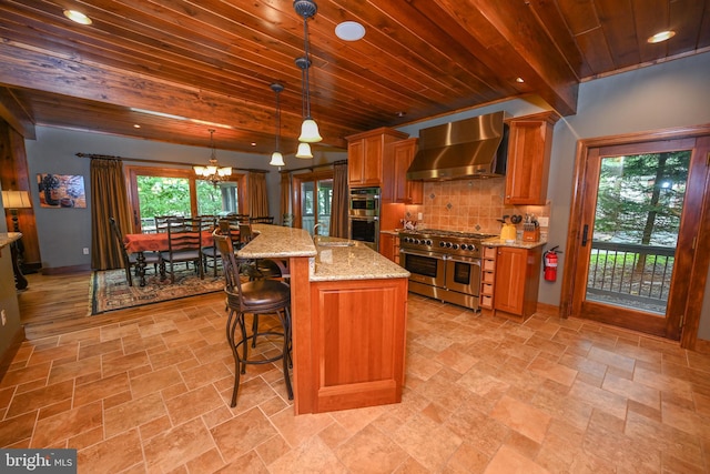 kitchen featuring wall chimney exhaust hood, hanging light fixtures, appliances with stainless steel finishes, beamed ceiling, and a center island