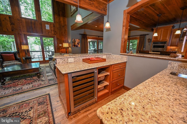 kitchen with wine cooler, brown cabinets, decorative light fixtures, stainless steel oven, and light stone countertops