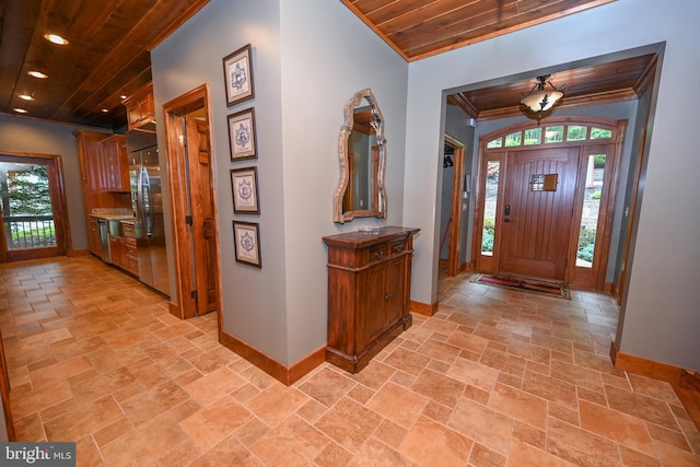 entryway featuring wooden ceiling, stone finish flooring, baseboards, and crown molding