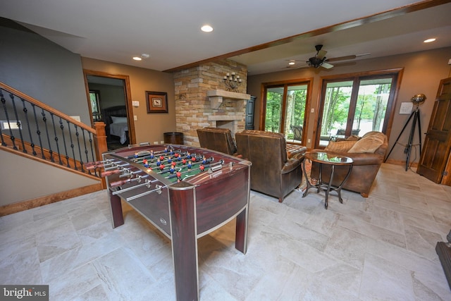 rec room with a ceiling fan, recessed lighting, a stone fireplace, and baseboards