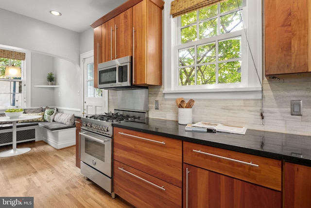 kitchen featuring radiator heating unit, tasteful backsplash, dark stone counters, stainless steel appliances, and light wood-type flooring