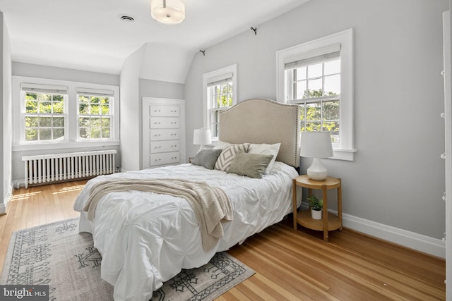 bedroom with multiple windows, radiator, and wood-type flooring